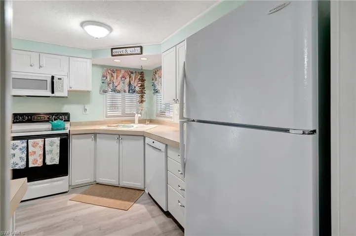 Kitchen with a textured ceiling, white appliances, sink, white cabinets, and light hardwood / wood-style floors