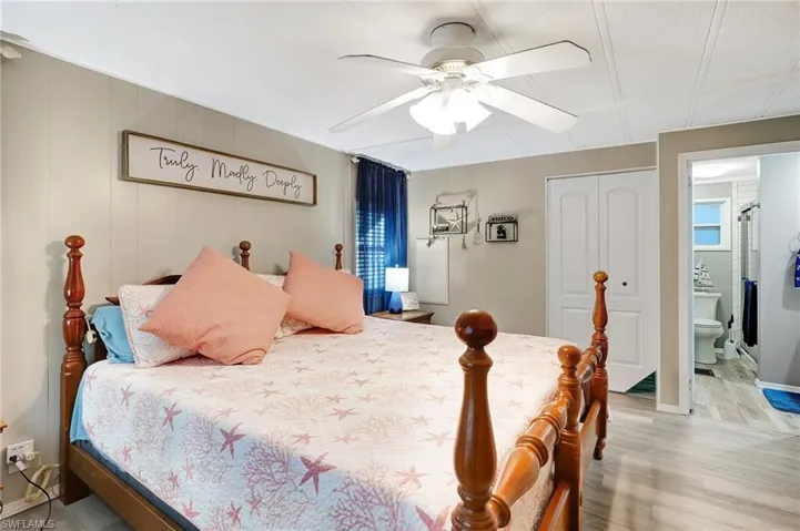Bedroom featuring connected bathroom, ceiling fan, light hardwood / wood-style floors, wooden walls, and a closet