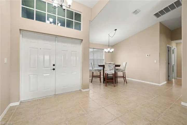 Double entry doors with transom window, tile flooring, vaulted ceilings, and a chandelier in the dining area