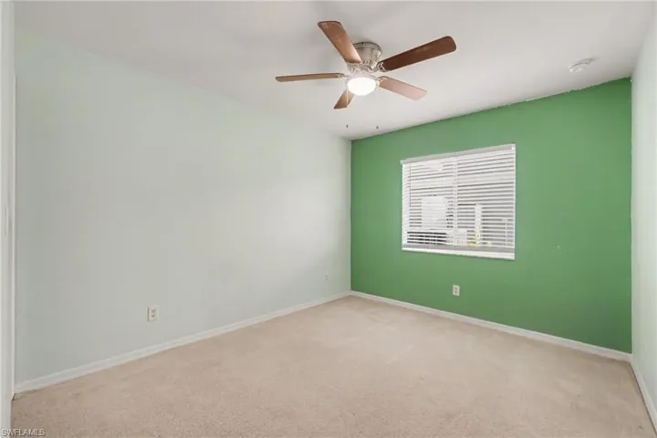 Carpeted room featuring a ceiling fan with integrated lighting, a window with horizontal blinds, and a contrasting accent wall