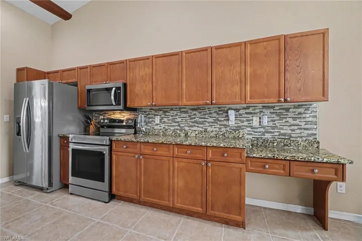 Kitchen featuring wood cabinetry, stainless steel appliances, granite countertops, and a tiled backsplash