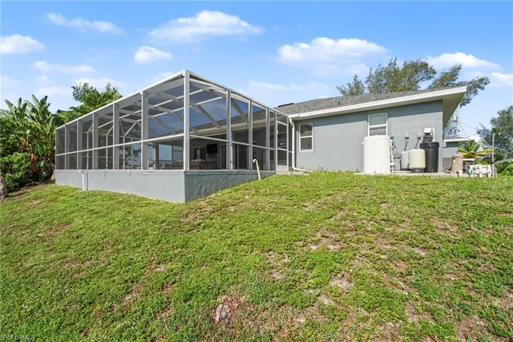Rear exterior featuring a large screened enclosure, stucco siding, and a sloped grassy area
