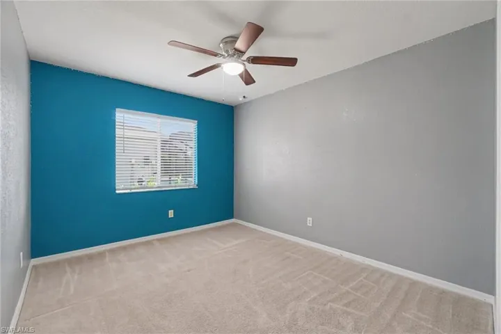 Room featuring a window with white blinds, a ceiling fan with light fixture, light neutral-toned carpet, and a blue accent wall