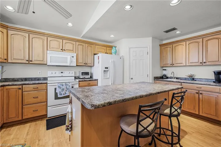 Kitchen featuring white appliances, light wood-type flooring, a kitchen breakfast bar, a kitchen island, and recessed lighting
