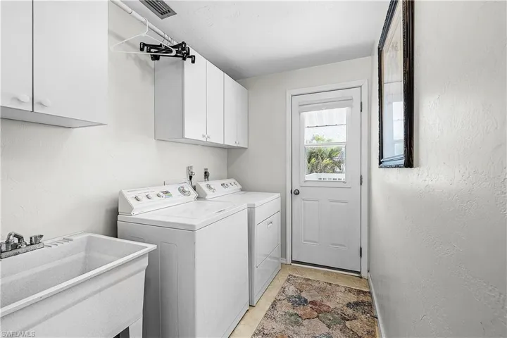 Laundry area featuring washing machine and dryer, cabinet space, a textured wall, and light tile patterned floors