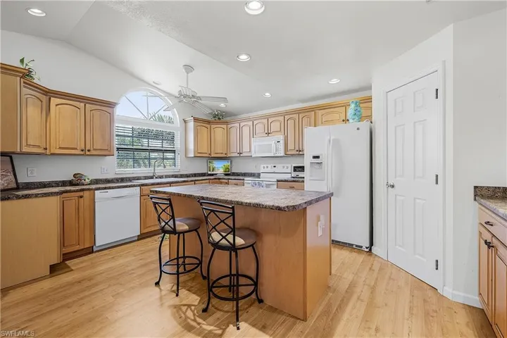 Kitchen featuring a kitchen bar, white appliances, light wood-type flooring, lofted ceiling, and recessed lighting