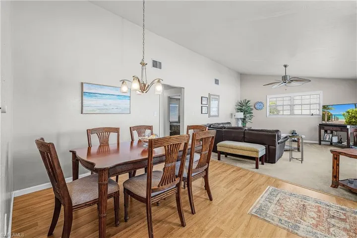 Dining space with light wood-style flooring, high vaulted ceiling, a ceiling fan, and a chandelier