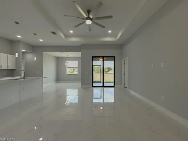 Empty room with a tray ceiling, a ceiling fan, visible vents, marble finish floor, and baseboards