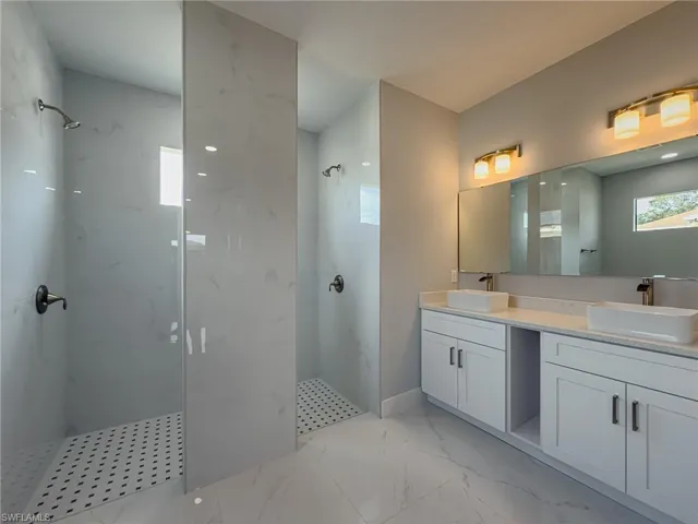 Full bath with a marble finish shower, double vanity, marble finish floor, and a sink