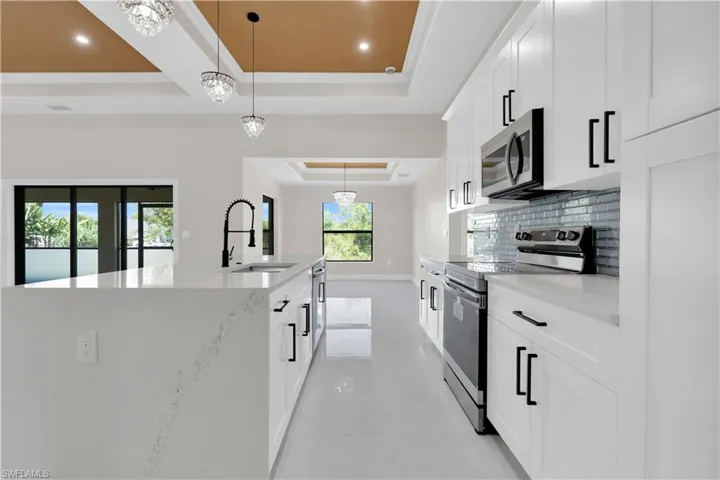 Kitchen with a tray ceiling, decorative light fixtures, appliances with stainless steel finishes, and white cabinets