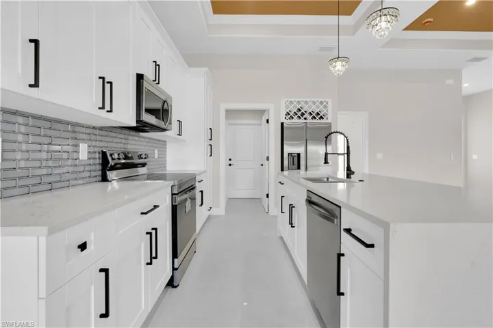 Kitchen with stainless steel appliances, light stone counters, pendant lighting, and backsplash