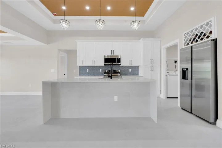Kitchen featuring stainless steel appliances, light stone countertops, tasteful backsplash, decorative light fixtures, and white cabinets
