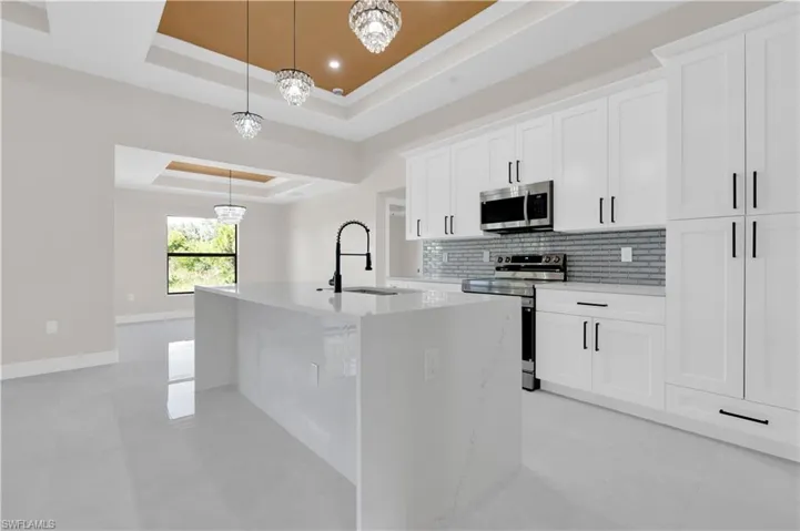 Kitchen featuring a raised ceiling, tasteful backsplash, pendant lighting, appliances with stainless steel finishes, and a kitchen island with sink