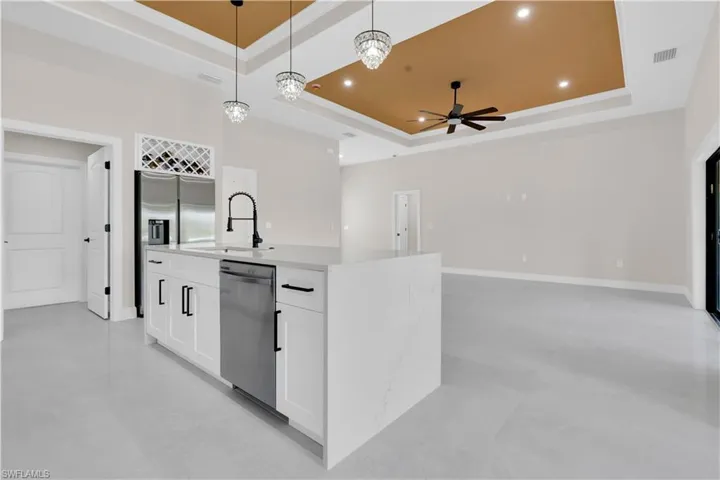 Kitchen with a tray ceiling, pendant lighting, white cabinetry, light stone countertops, and a center island with sink