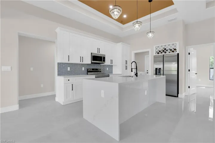 Kitchen with decorative backsplash, stainless steel appliances, white cabinetry, pendant lighting, and light stone counters