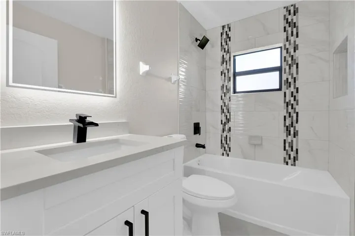 Bathroom with a textured wall, bathtub / shower combination, and vanity