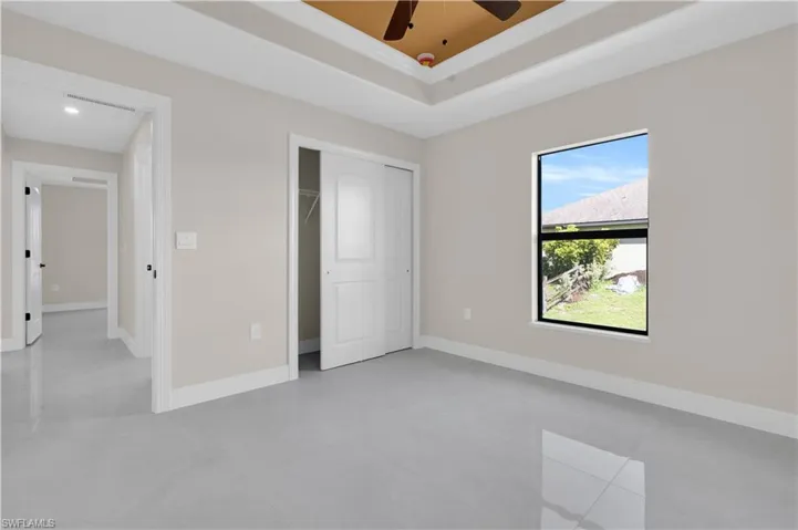 Unfurnished bedroom with a tray ceiling, ceiling fan, a closet, and light tile patterned floors