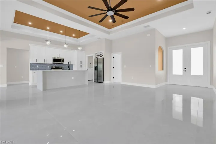 Unfurnished living room with a tray ceiling, french doors, recessed lighting, a ceiling fan, and arched walkways