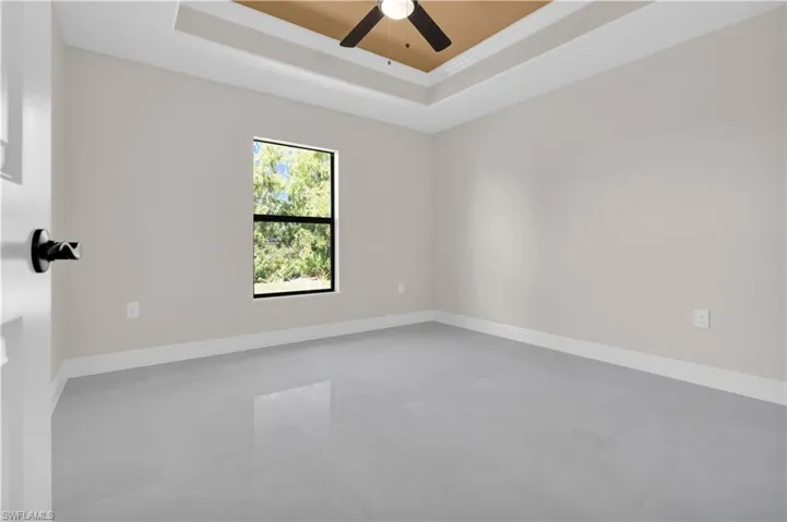 Empty room with a tray ceiling, a ceiling fan, and ornamental molding