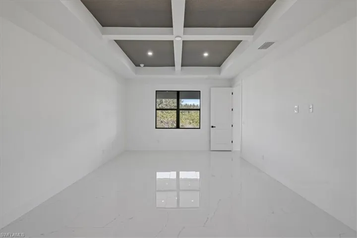 Spare room featuring coffered ceiling, light marble finish floors, and recessed lighting