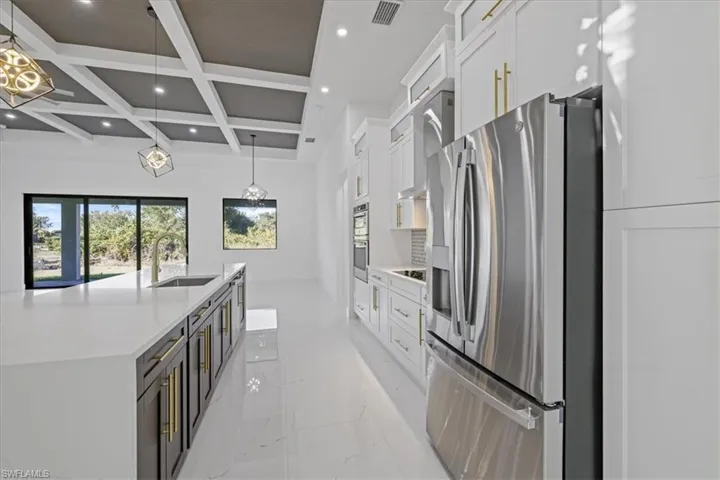 Kitchen featuring coffered ceiling, stainless steel appliances, two tone cabinetry, light stone counters, and light marble finish floors