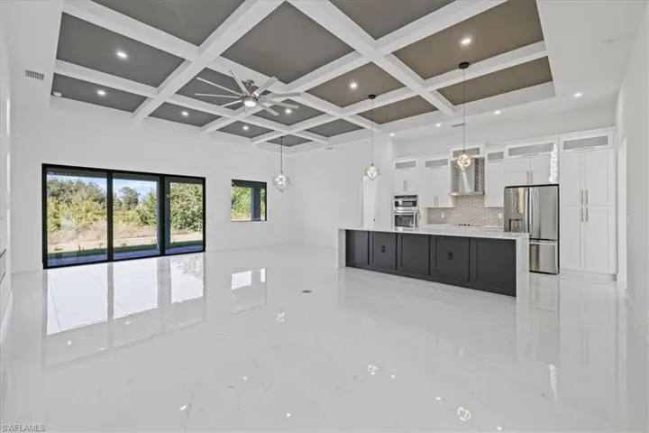 Dual tone kitchen with glass insert cabinets, decorative light fixtures, open floor plan, stainless steel appliances, and a large island with sink