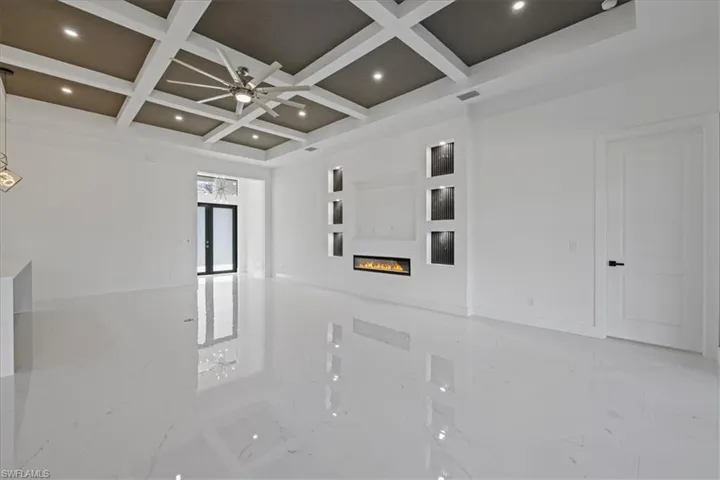 Empty room featuring a glass covered fireplace, a ceiling fan, coffered ceiling, and recessed lighting