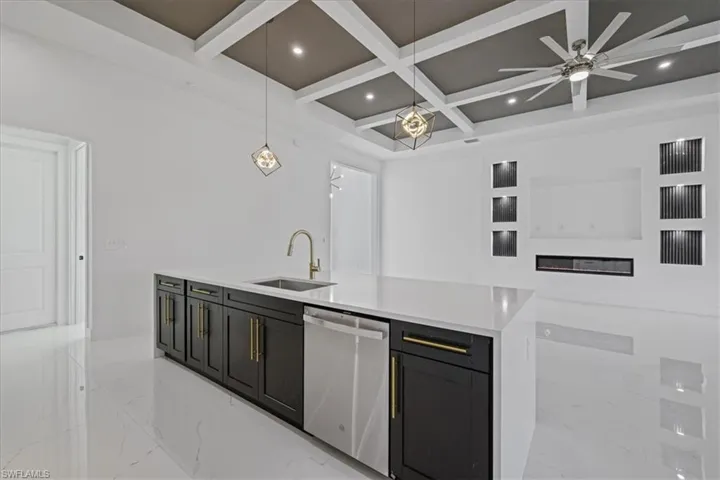 Kitchen featuring pendant lighting, dark cabinetry, coffered ceiling, light stone counters, and stainless steel dishwasher