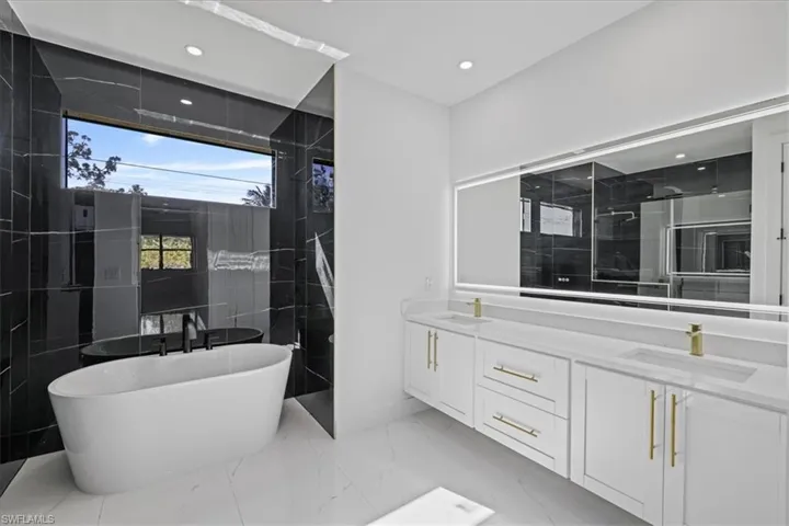 Bathroom featuring double vanity, a freestanding bath, walk in shower, recessed lighting, and light marble finish flooring
