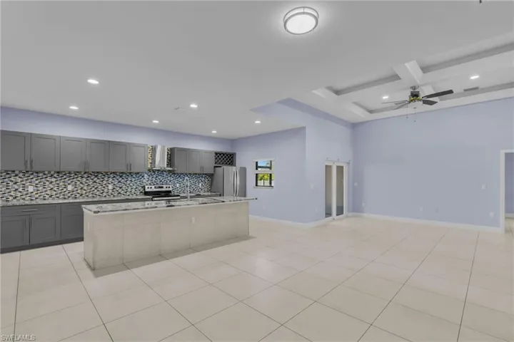 Kitchen with decorative backsplash, wall chimney range hood, a kitchen island with sink, and stainless steel appliances