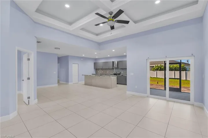 Unfurnished living room featuring beam ceiling, ceiling fan, light tile patterned floors, and coffered ceiling