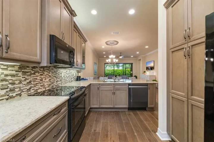 Kitchen featuring black appliances, crown molding, light stone countertops, a chandelier, and dark wood-style flooring