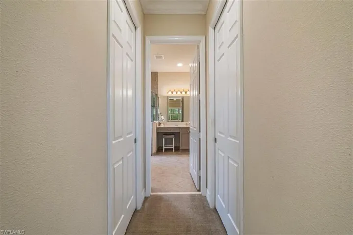 Hallway with a textured wall, dark carpet, and crown molding