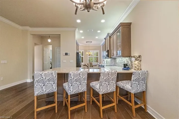 Kitchen featuring a chandelier, light stone countertops, a breakfast bar, glass insert cabinets, and pendant lighting