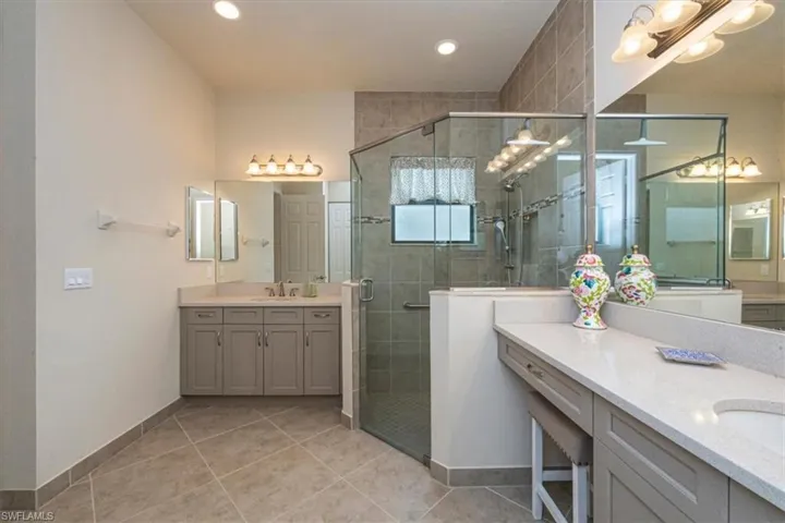 Full bath with two vanities, a shower stall, and light tile patterned floors
