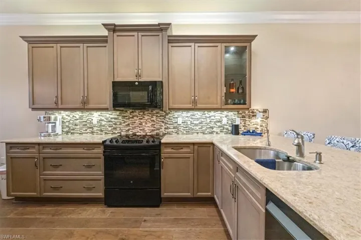 Kitchen with black appliances, light stone countertops, glass insert cabinets, light wood-type flooring, and crown molding
