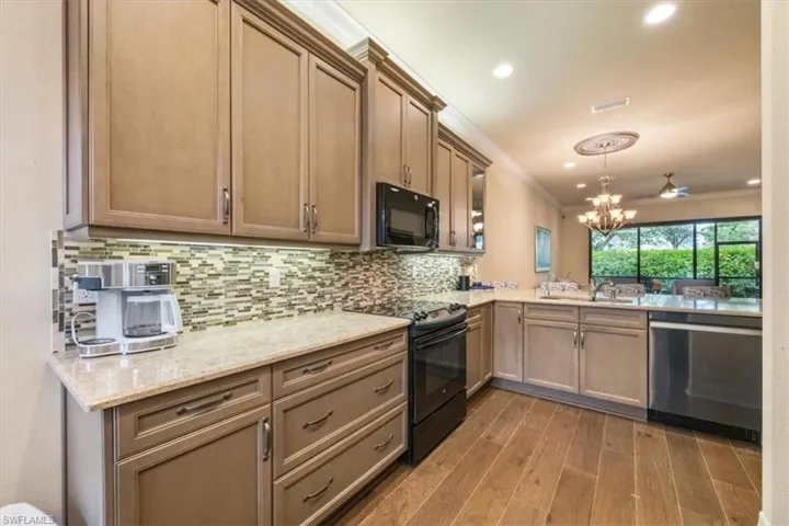 Kitchen with black appliances, pendant lighting, ornamental molding, light wood-style flooring, and light stone countertops