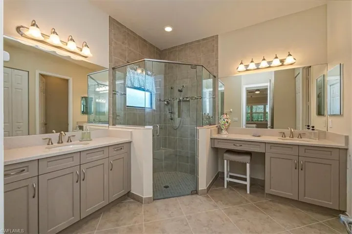 Full bath featuring two vanities, a stall shower, light tile patterned floors, a closet, and healthy amount of natural light