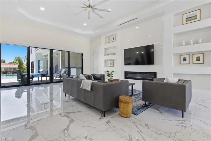 Living room featuring built in shelves, light marble finish flooring, recessed lighting, and a tray ceiling