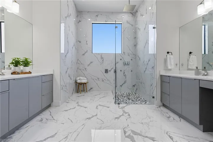 Bathroom with light marble finish flooring, a marble finish shower, and two vanities