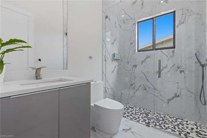 Full bath featuring vanity, a marble finish shower, and light marble finish floors