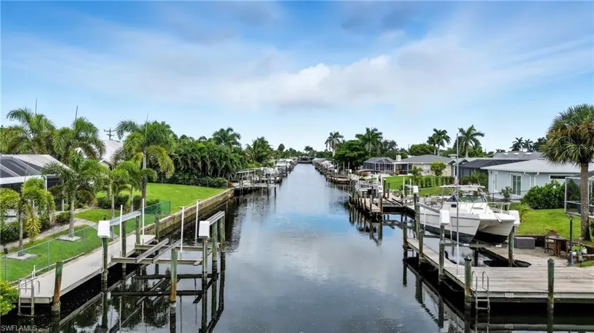 Dock area with boat lift, a water view, a residential view, and a lawn