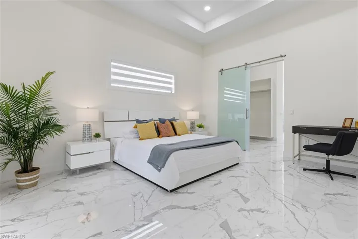 Bedroom featuring a walk in closet, light marble finish floors, a barn door, recessed lighting, and a tray ceiling