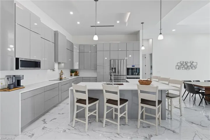Kitchen featuring gray cabinets, modern cabinets, a kitchen breakfast bar, light marble finish floors, and hanging light fixtures