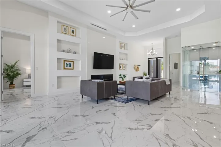 Living area featuring built in features, a tray ceiling, a chandelier, light marble finish floors, and recessed lighting