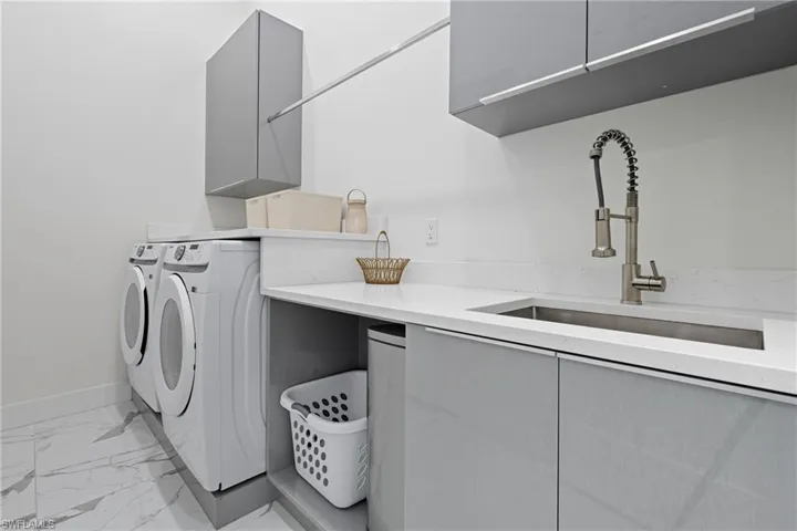 Laundry area featuring light marble finish floors, cabinet space, and washing machine and clothes dryer