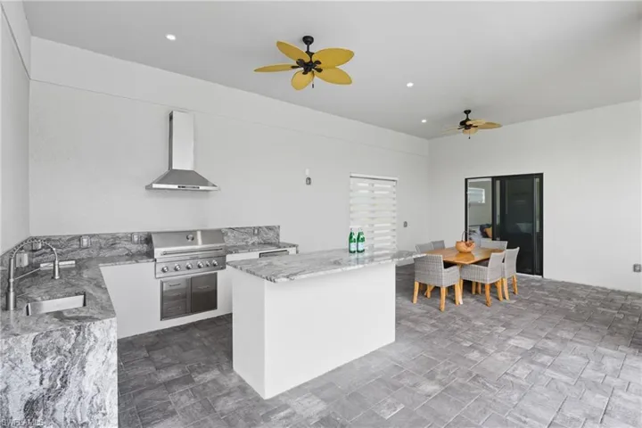 Kitchen with light stone countertops, wall chimney range hood, a ceiling fan, recessed lighting, and white cabinets