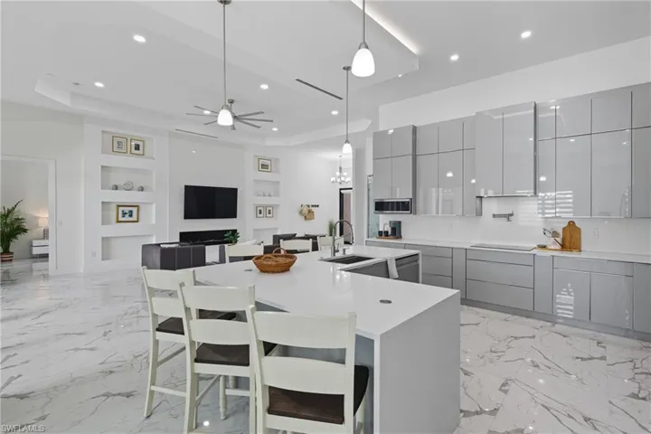 Kitchen with gray cabinets, a kitchen bar, pendant lighting, a raised ceiling, and recessed lighting