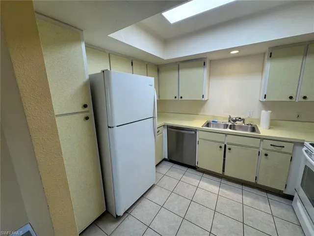 Kitchen featuring a tray ceiling, white refrigerator and range, dual basin stainless steel sink, light-toned countertops, and tile flooring