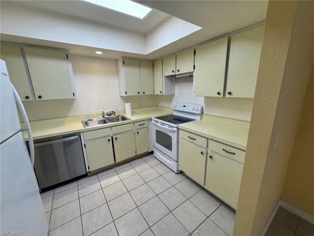 Kitchen with a tray ceiling and light, white tile flooring, ample cabinetry, a double basin stainless steel sink, and a stainless steel dishwasher
